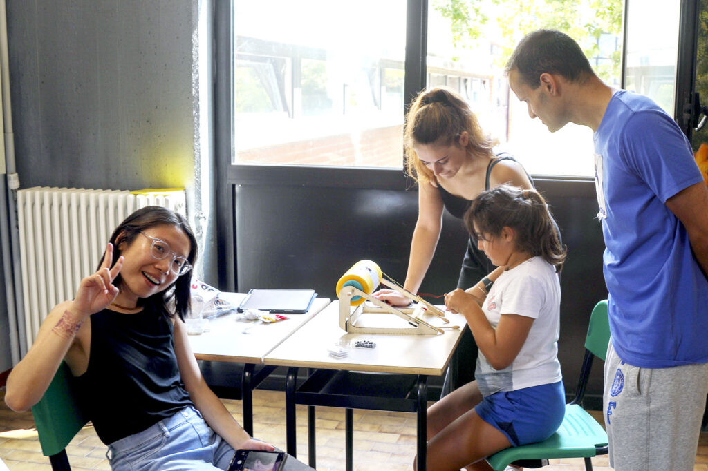 A group of adults watching a young girl playtest a mini tombolo kit.